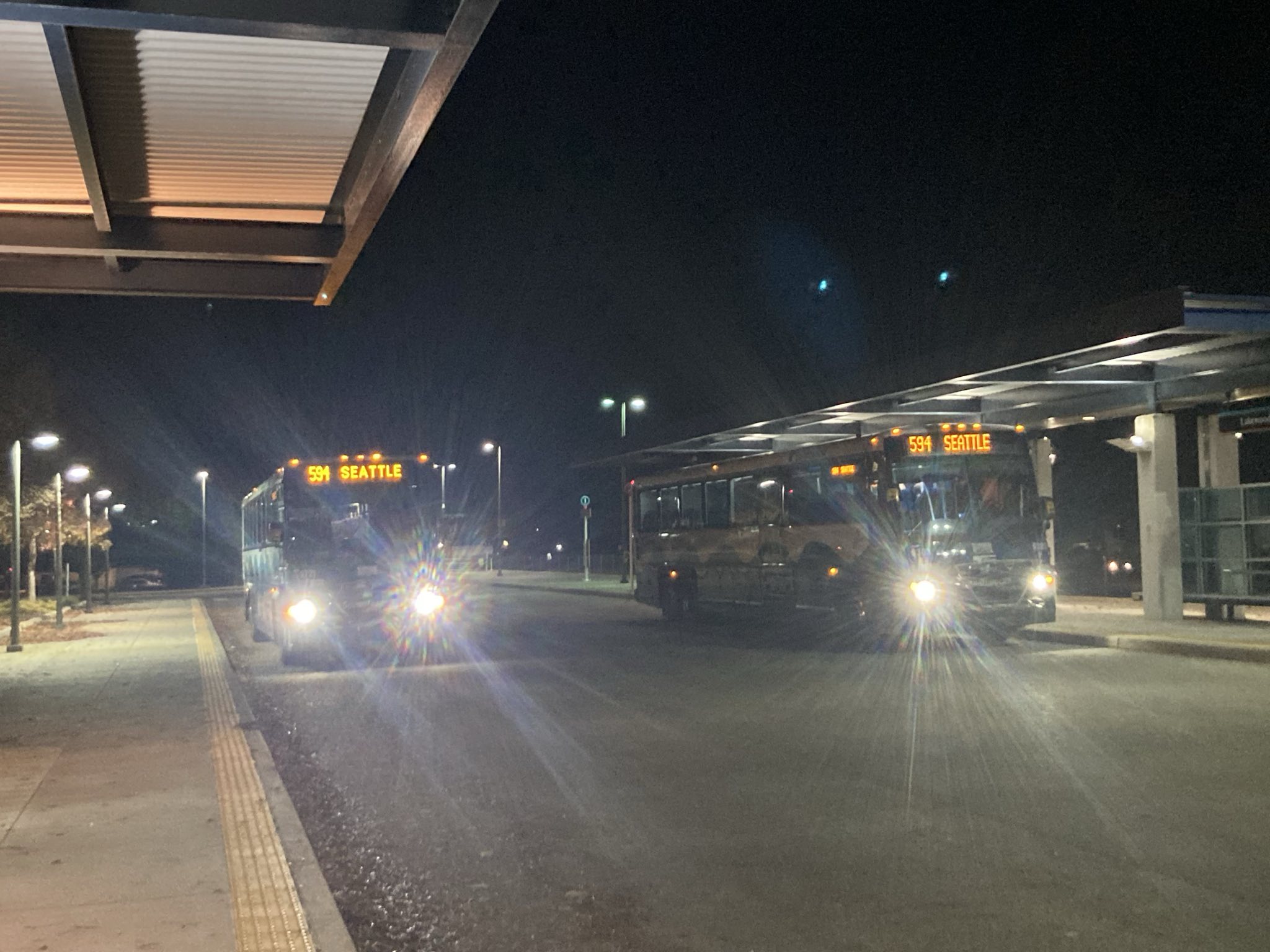 Night photo showing two Sound Transit MCI buses, both claiming to be the 594 to Seattle